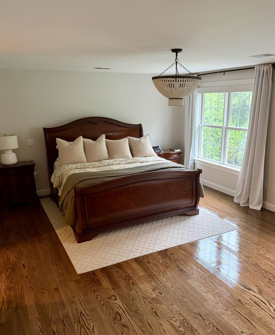 A freshly cleaned primary bedroom with polished hardwood floors and morning light